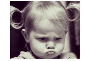 A young child with pigtails and a pouty expression looks directly at the camera, embodying a sulky demeanor in a black-and-white photograph.