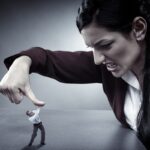 A small man in a suit struggles to push against a giant hand pressing down on him, symbolizing overwhelming pressure and power dynamics.